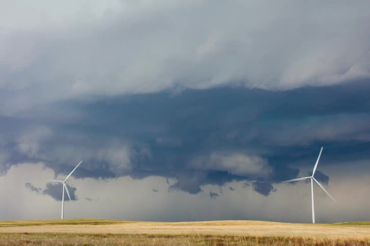 Storm clouds gathering over a field with two modern windmills