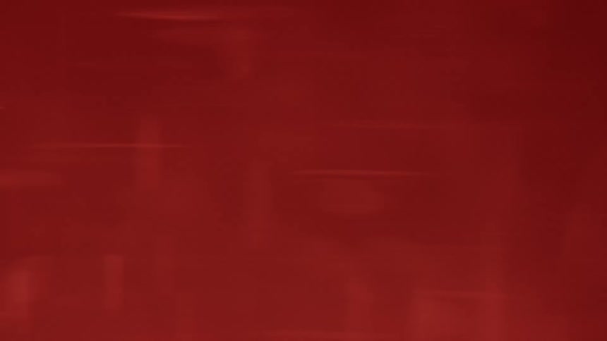 The video displays an abstract solid red background with subtle light flares and a grainy texture the light flares which appear as thin horizontal and circular beams briefly move across the screen