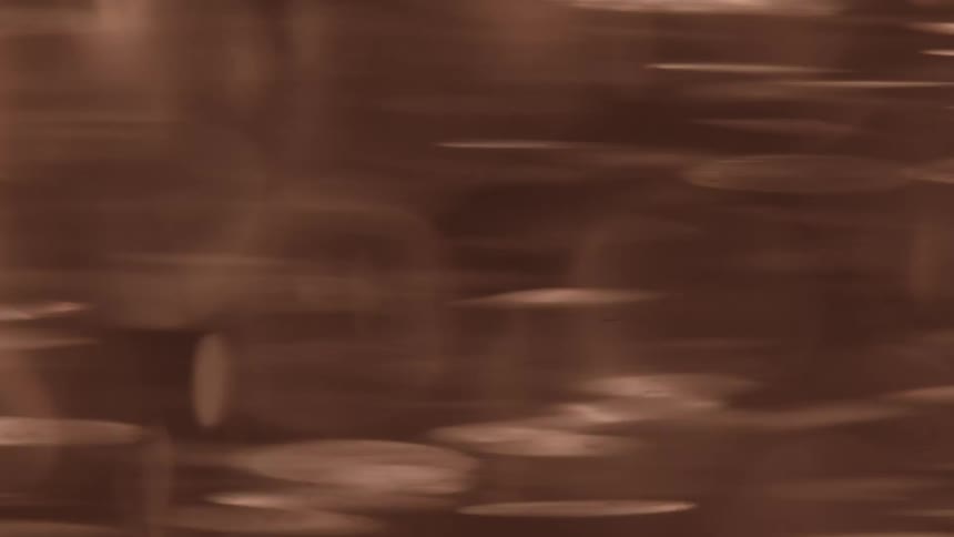 The video shows a blurry abstract background with a brownred color palette the light flares within the frame are out of focus appearing as bokeh effects that rapidly move horizontally across the screen