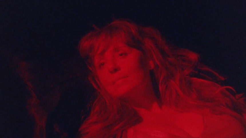 A closeup shot of a woman with a red filter over the camera with the person looking into the camera while their face is illuminated