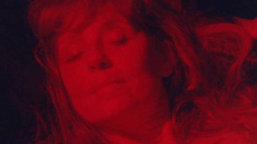 A woman lying down smiles as she turns her head to one side of the pillow then another under heavy red light
