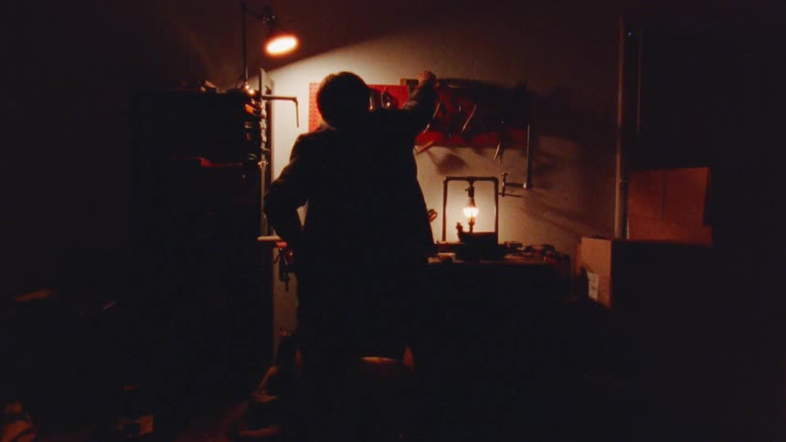 Silhouette of a man sitting down working with tools on a tool shed indoors