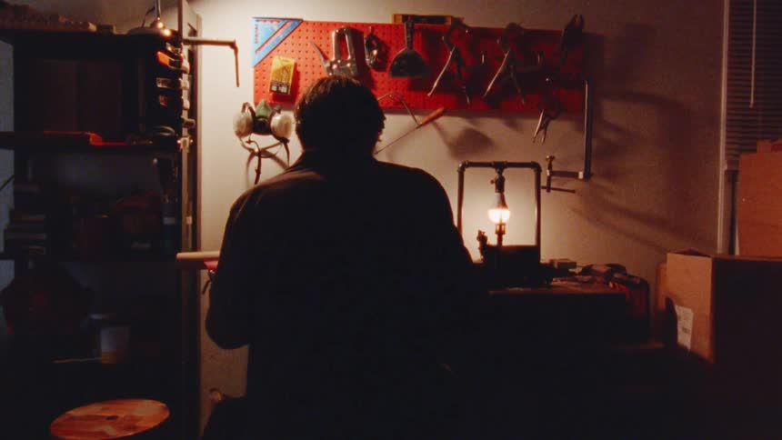 A persons silhouette working at a workbench in a cluttered workshop with the only light source coming from a table lamp