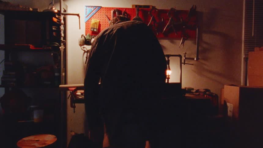Person works at a lit workbench surrounded by tools on the wall
