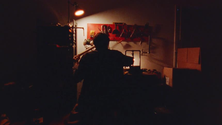 A persons silhouette working at a workbench in a cluttered workshop with a bright glow illuminating the scene as he grab a tool