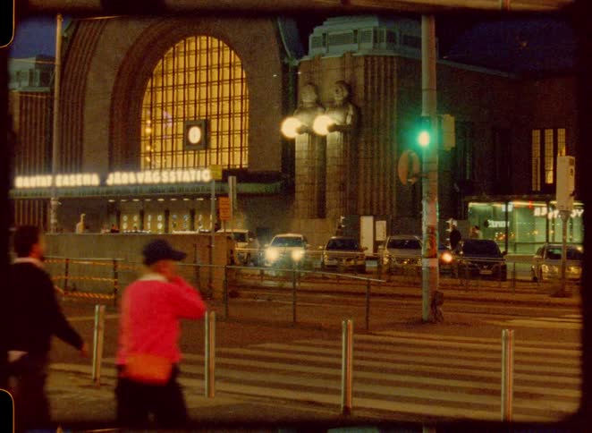 A group of people crossing the road at a zebra crossing in the city at night with the traffic light green and other cars waiting