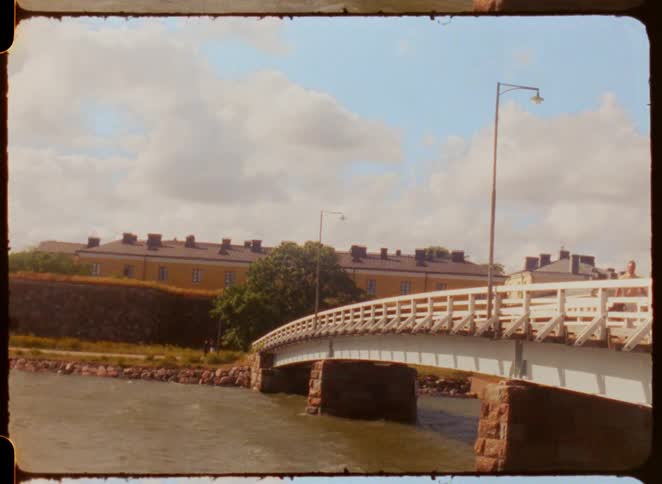 Two adult men walking over a bridge over a river next to a building outdoors during day time