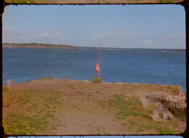Grassy area ends at a cliff facing the sea with a red rescue pole
