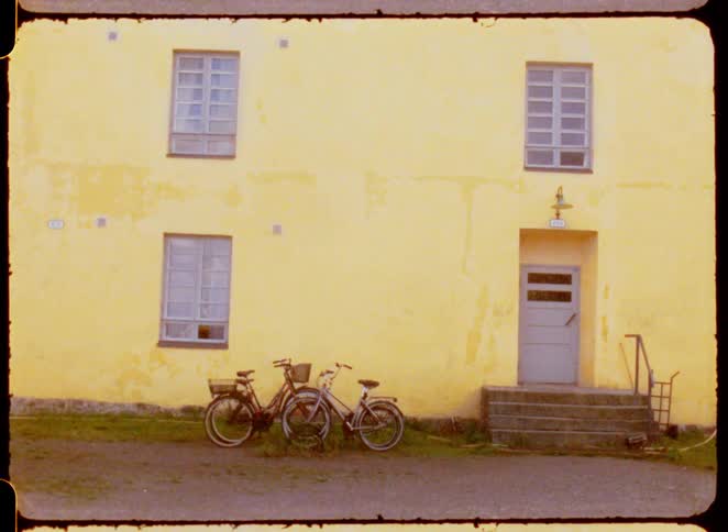 Bicycles parked next to the door of a yellow building outdoors during day time