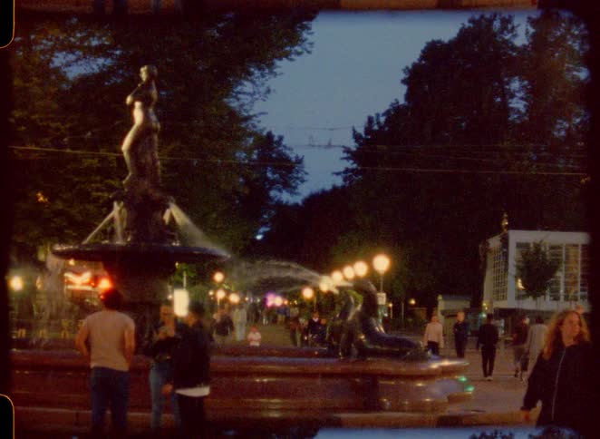 The bus passes a fountain in the park full of people