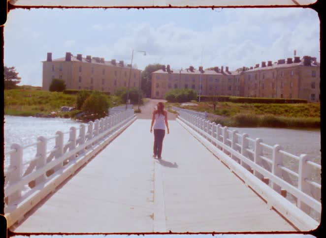 The woman walks over the bridge towards the row of buildings