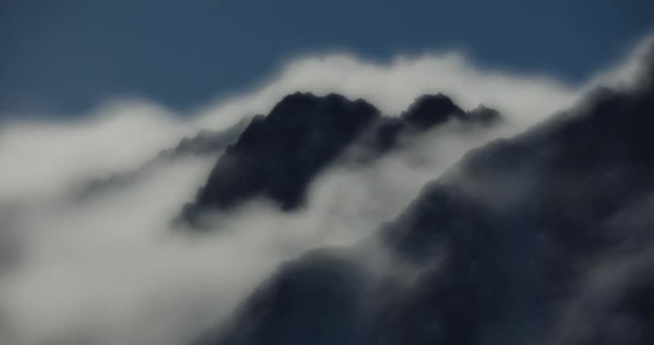 Thick clouds moving across a landscape revealing and then obscuring rugged dark mountain peaks