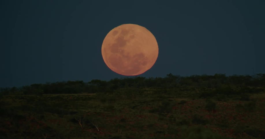 A full moon glows brightly above the dark hillside at night