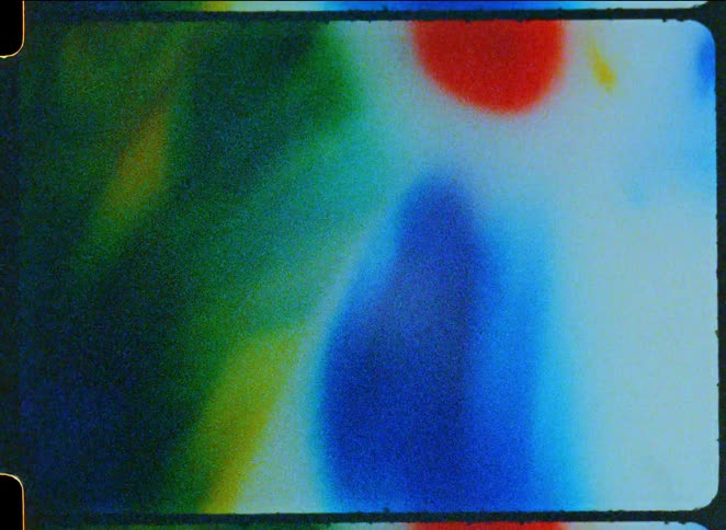 This clip displays a grainy abstract texture reminiscent of a damaged or overexposed vintage film strip soft outoffocus patches of blue green and red bleed into one another creating a dreamy retro aesthetic