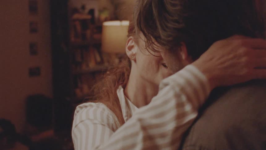 A blonde woman kissing and hugging a bearded man indoors