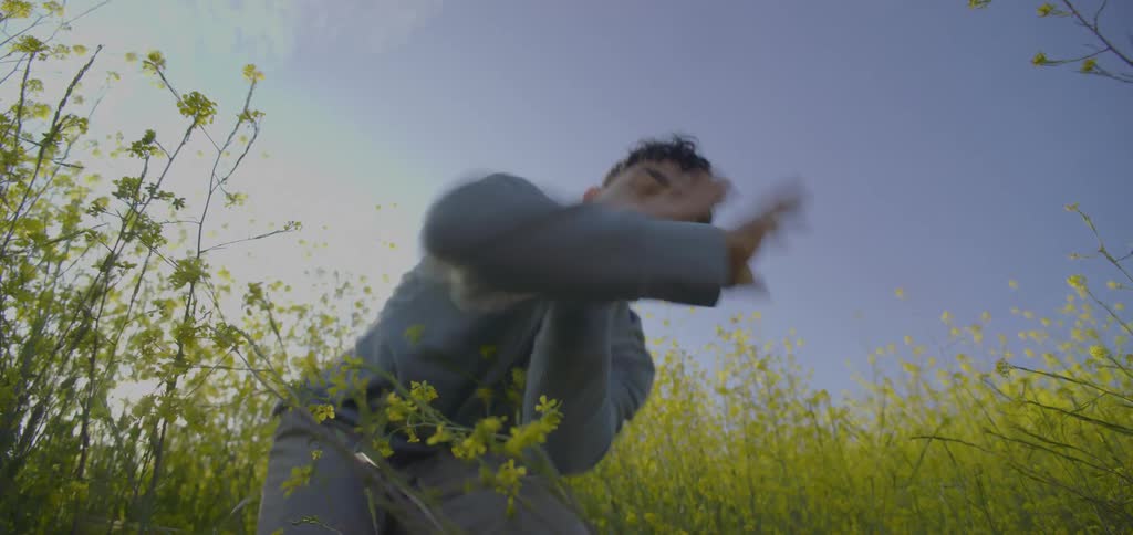 A young man in the bush at midday dancing with kung fu moves while wearing a sweatshirt