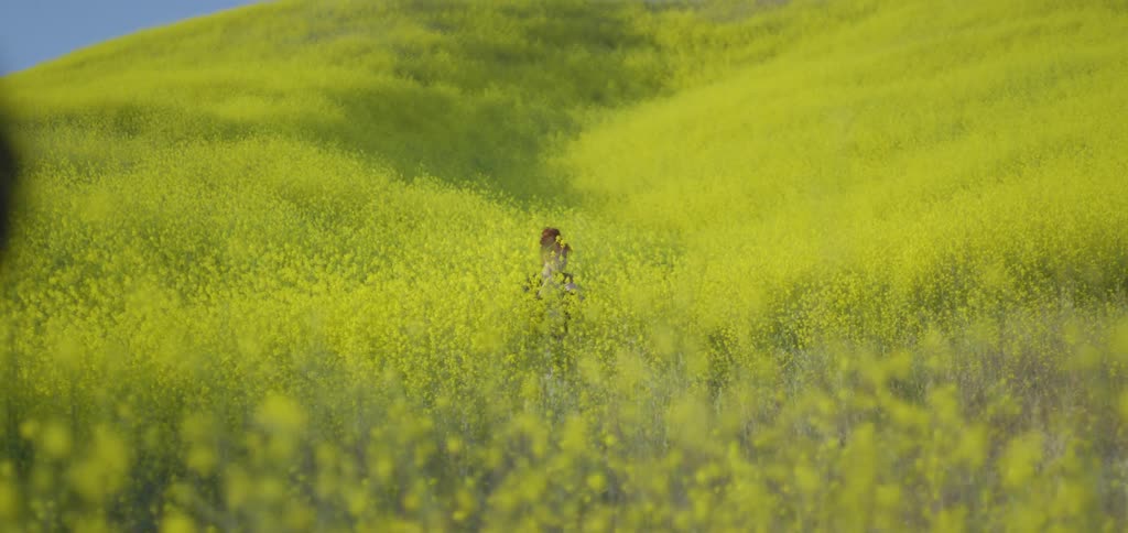 A young man standing on a grassland with a woman behind him among tall grass and bushes changing her clothes at midday