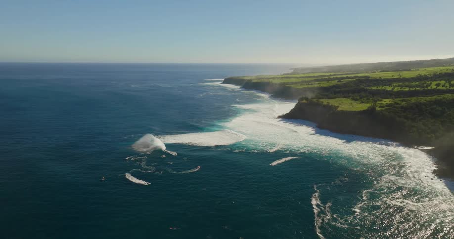 A massive wave crashing against a lush green cliffside creating a large majestic plume of spray and foam