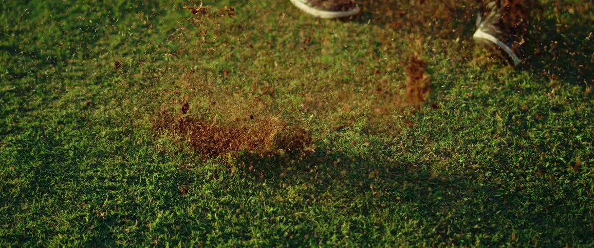 A person swinging a golf club on a golf course scattering grass as the ball is hit at midday