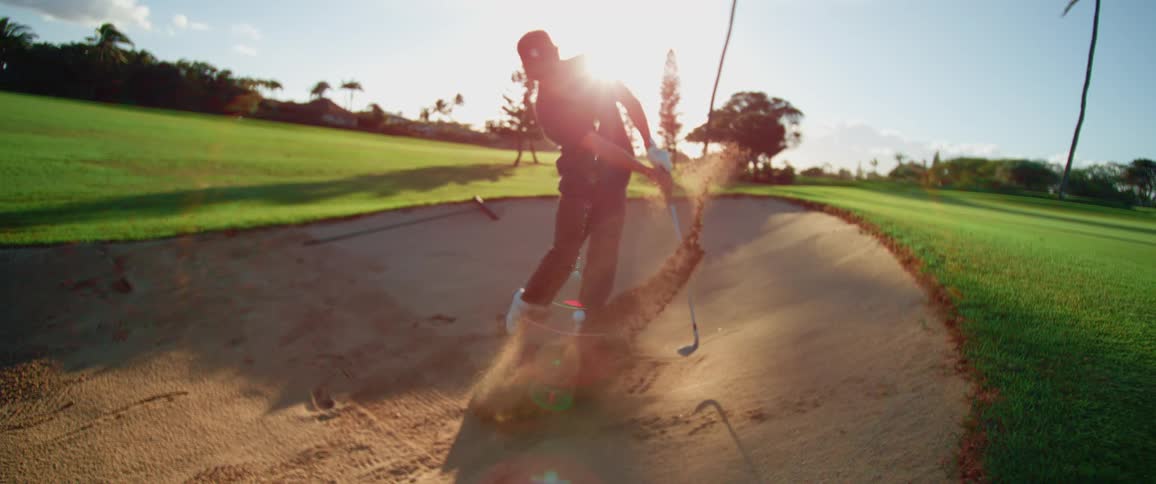 A golfer hits the ball from a sand bunker on a sunny course