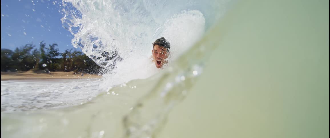 Man slides excitedly on a wave breaking near the beach
