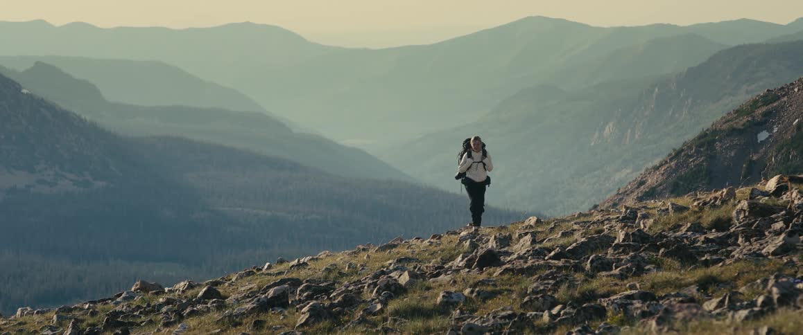 Female hiker walks across a rock strewn slope above a foggy valley