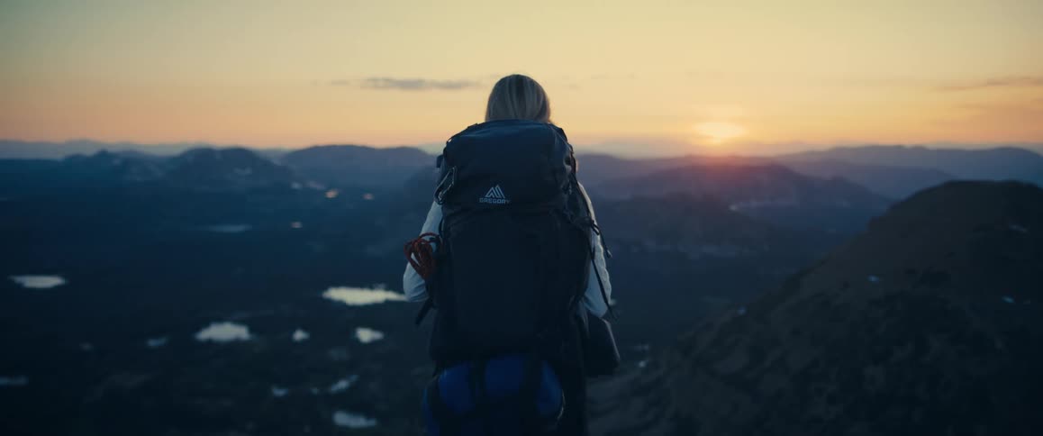 Person with a hiking backpack watches the sunset over the mountains