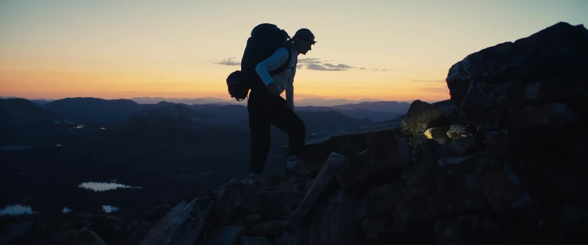 A hiker with a headlamp climbs rocky terrain at sunset