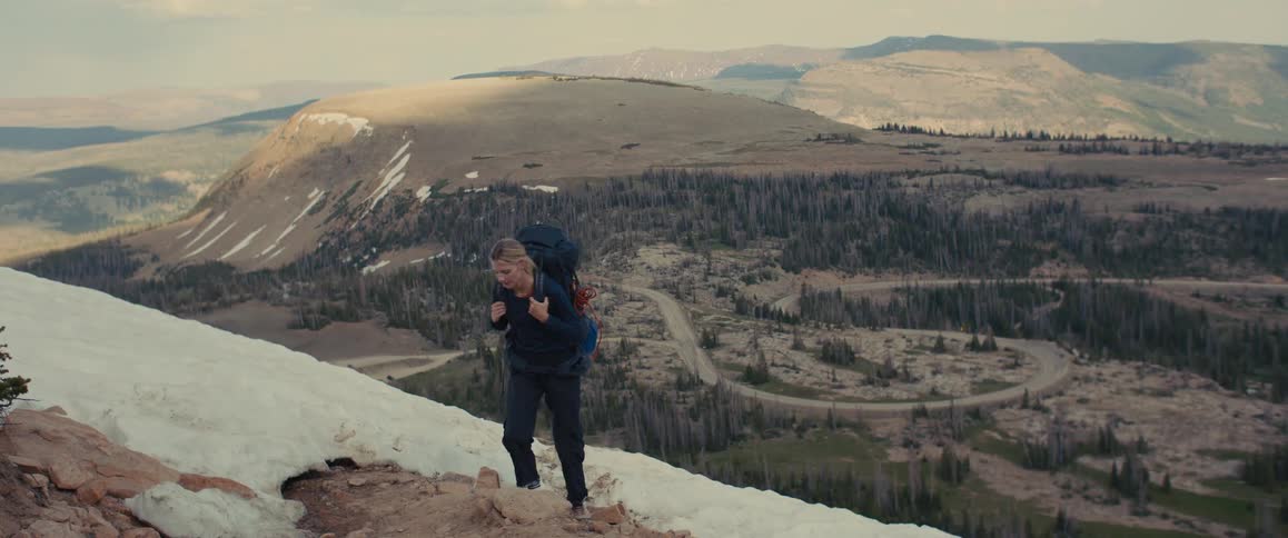 A hiker climbs a snowy mountain slope with a valley view below
