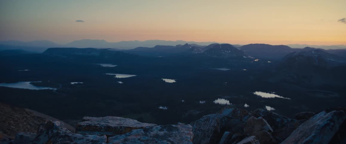 Mountain range surrounded by a flat land with vegetation and streams and another mountain range on the background outdoors during dusk or dawn