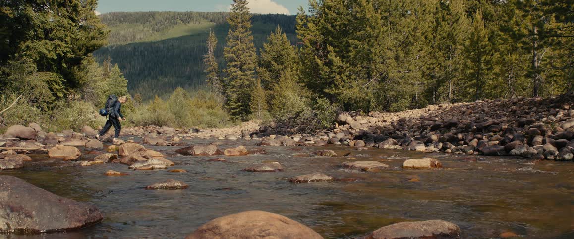 Female backpacker picks her way across a river in the woods