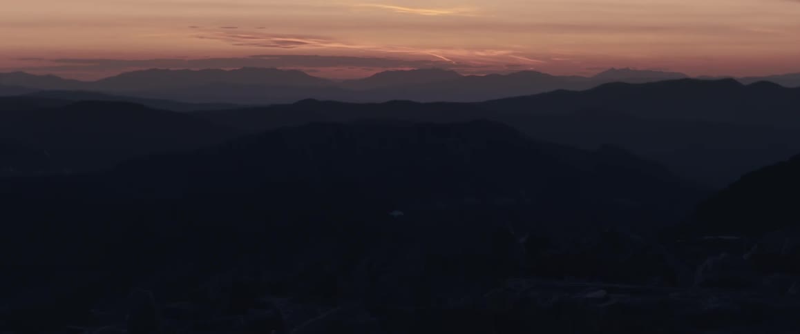 Silhouettes of mountains across the landscape under a cloudy sunset sky