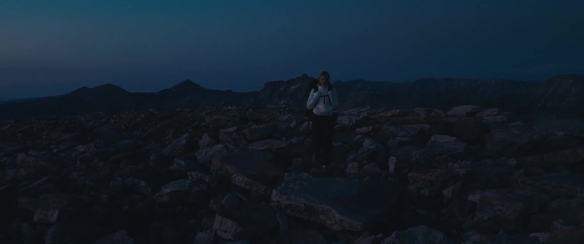 A hiker walks across a rocky mountain terrain at dusk