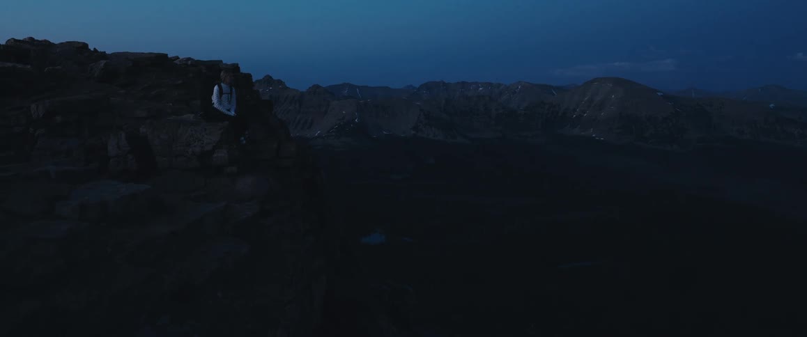 Woman sitting on a rock by a mountain trail on a dark dawn