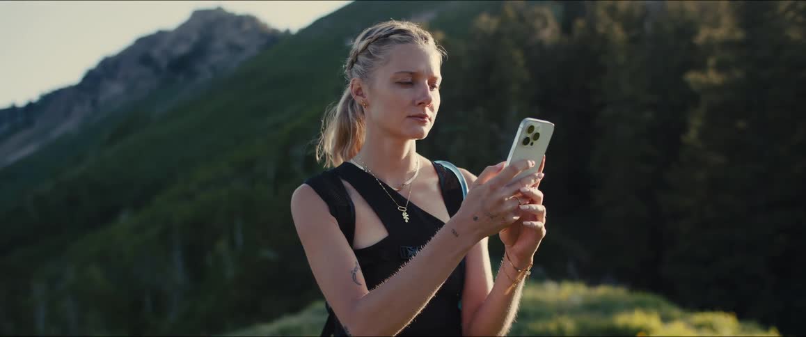 A female hiker with a braided ponytail stops on a mountain checking her phone and walking away