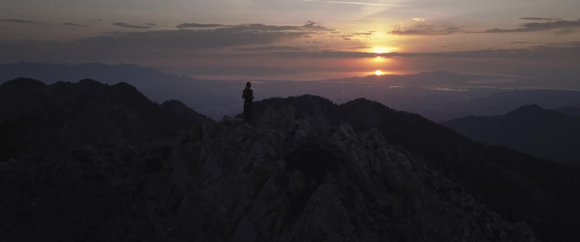 A person silhouetted against a beautiful sunset standing on a rocky mountain ridge