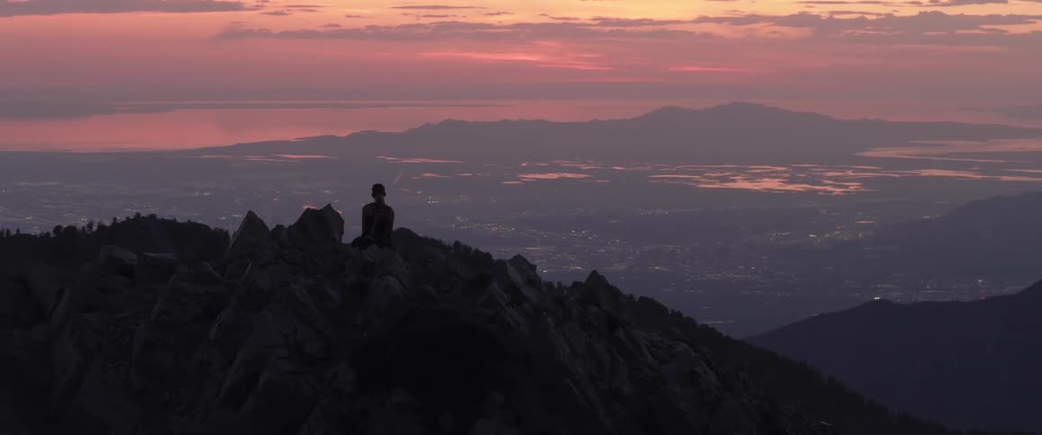 A person sitting on a rocky mountaintop silhouetted against a sunset