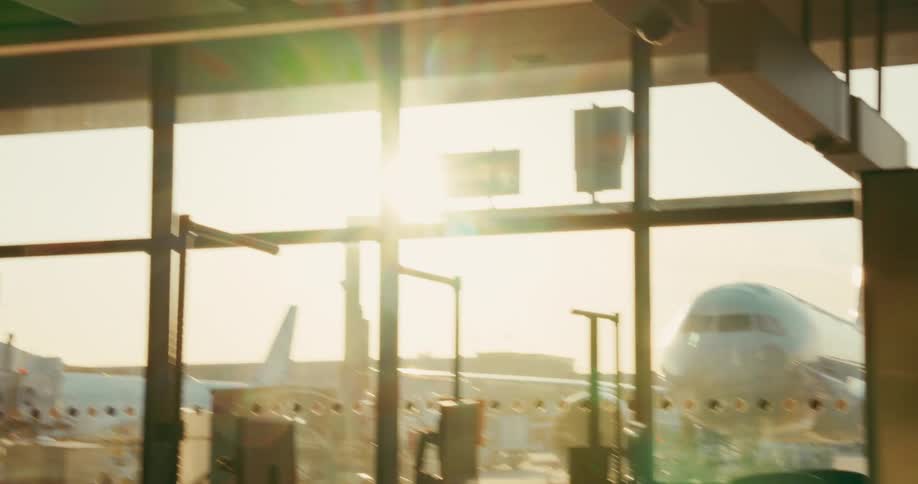 Sunlight and lens flare fill airport windows revealing a parked airplane behind frames and structures