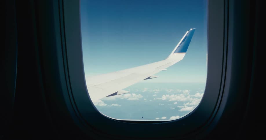 Wing of an airplane flying on the sky seen through the shuttle during day time