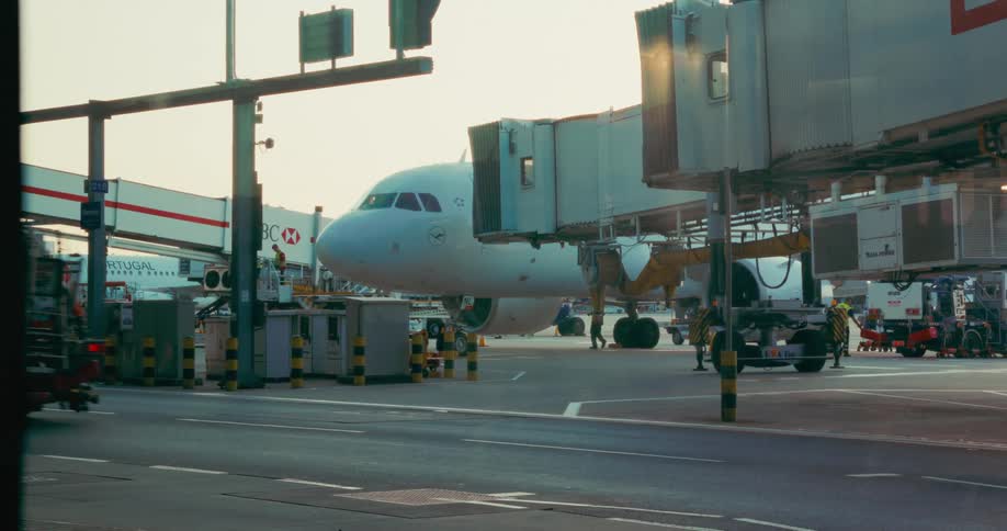 Service truck driving by a parked airplane surounded by boarding stairs and working people at an airfield outdoors during day time