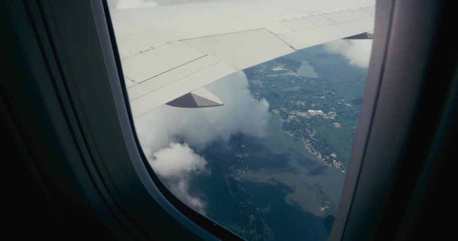 A white wing above a scattered cloud revealing a landscape of green land several bodies of water and residential areas below