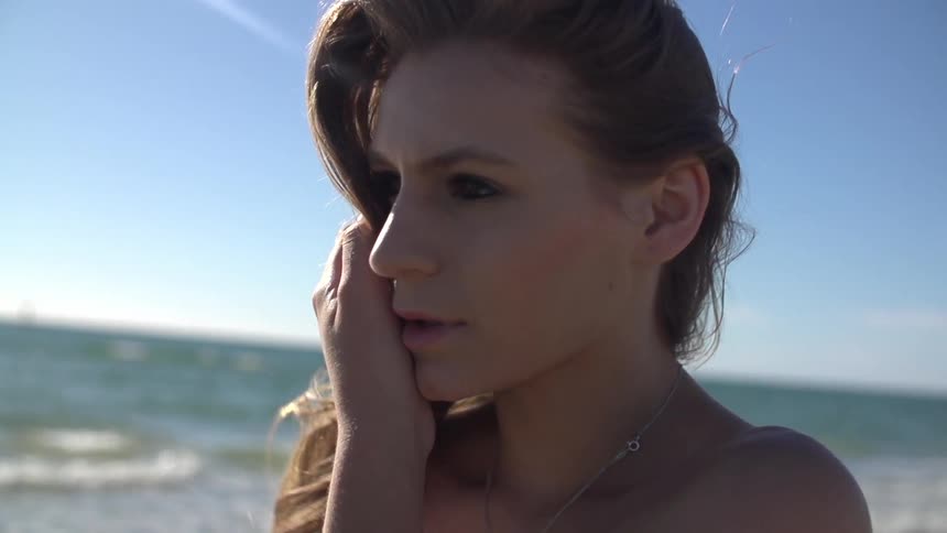 A beautiful young woman turns toward the camera on a bright, sunny day at the beach