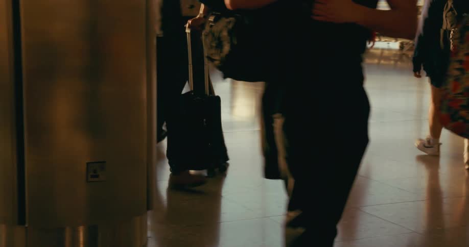 Large group of people walking and carrying luggage indoors on an airport area during dusk or dawn