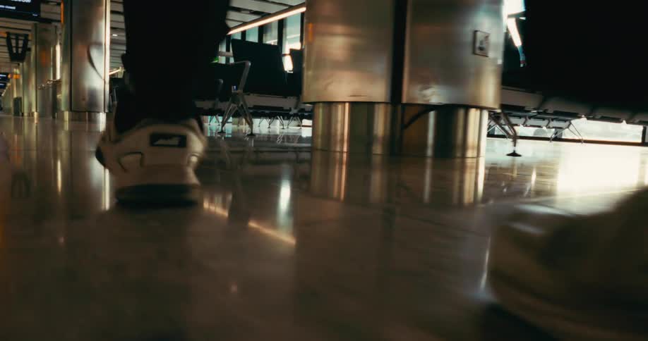 A ground level view follows a persons feet in white and black sneakers as they walk quickly through a clean polished airport terminal