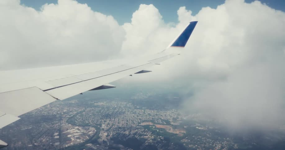 An airplane wing seen from a window flying above the city and clouds