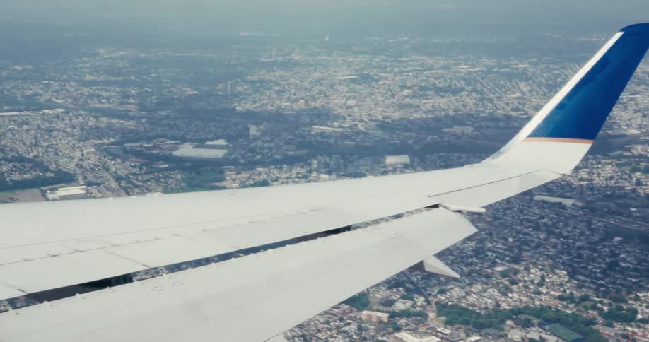 Wing of an airplane flying low over an urban area outdoors during day time