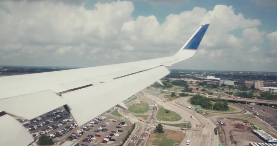 Wing of an airplane flying low over a city and arriving at an airport outdoors during day time
