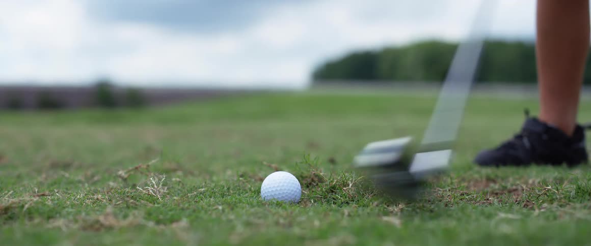 Person hitting a golf ball on a grass course during the day