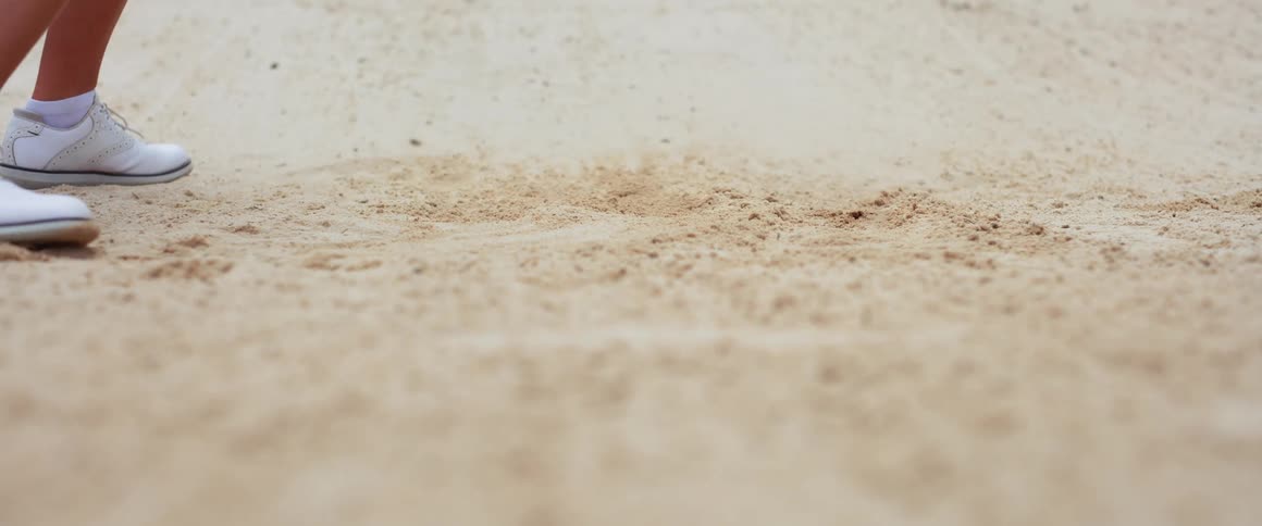Golf club hits the sand raising particles during the shot