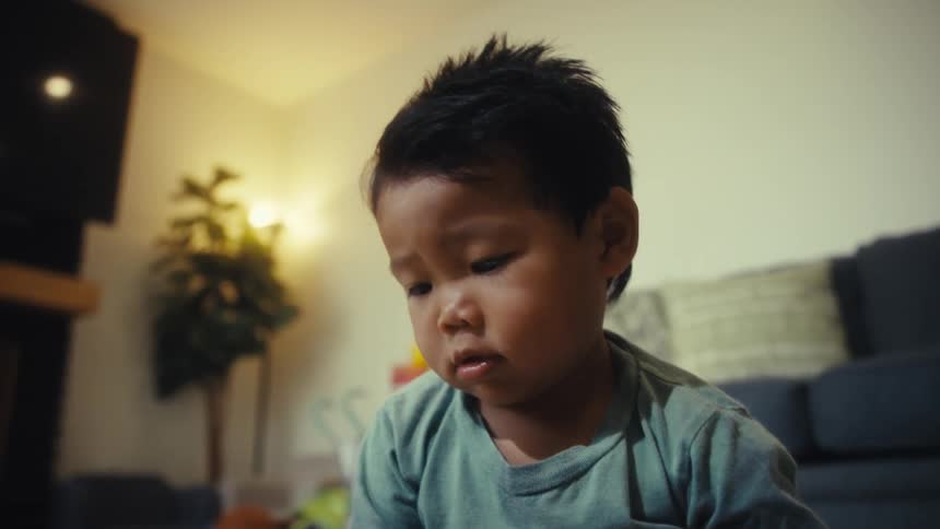 Male toddler looking at the floor and frowning indoors next to another person